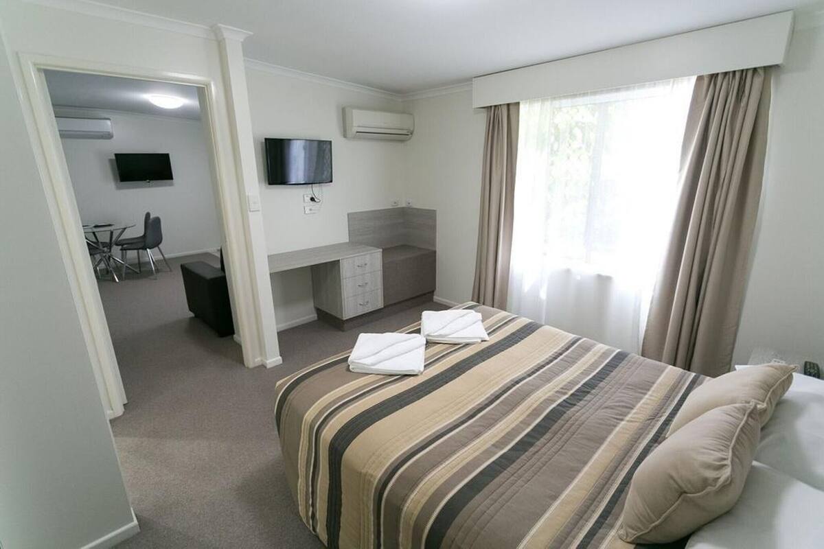 Habitación de hotel con cama, escritorio, silla, televisor y ventana con cortinas.