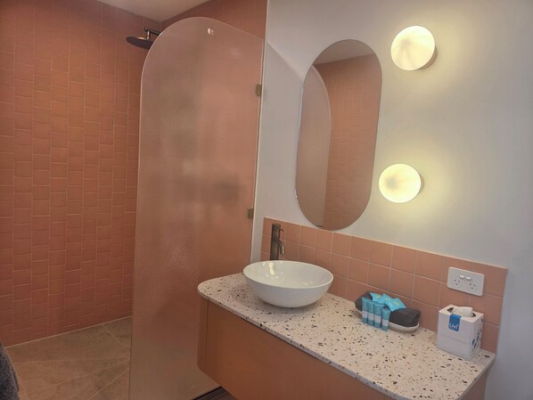 A bathroom with a large mirror, a sink with a bowl, toiletries, and a shower area.