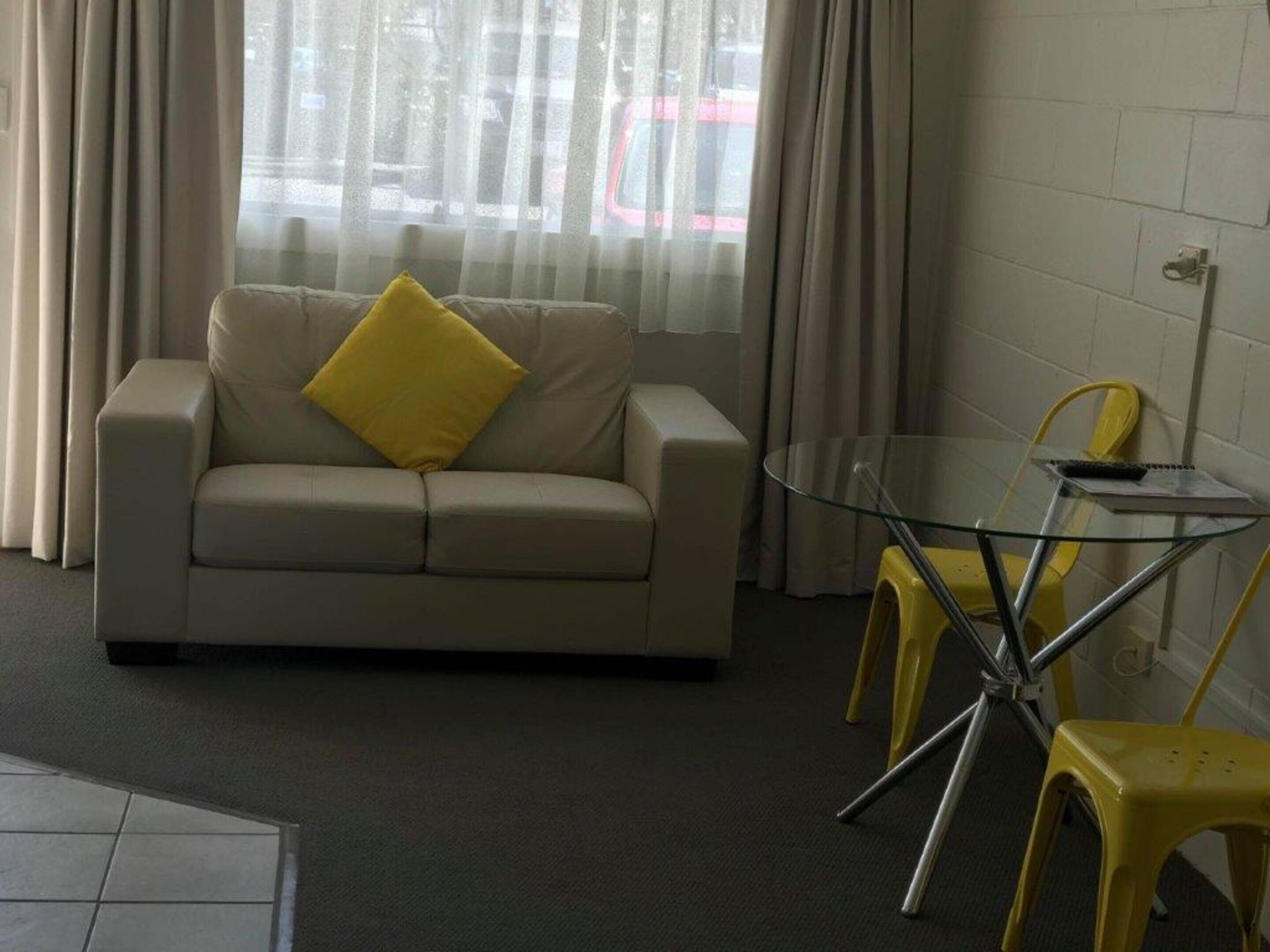 A living room with a beige sofa, a glass coffee table, and yellow chairs.