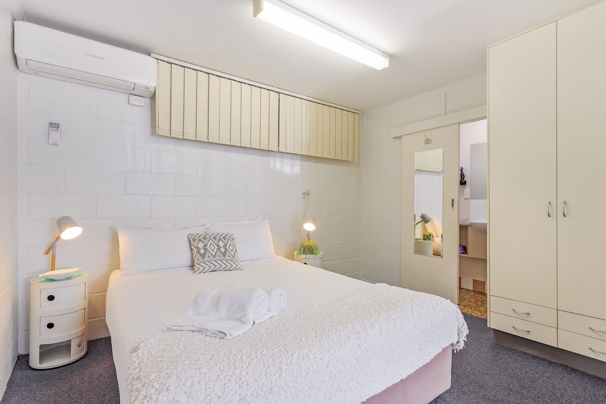 A hotel room with a bed, bedside lamps, a wardrobe, and a mirror.