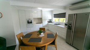 A modern kitchen with white cabinets, a stainless steel refrigerator, and a dining area with a wooden table and chairs.