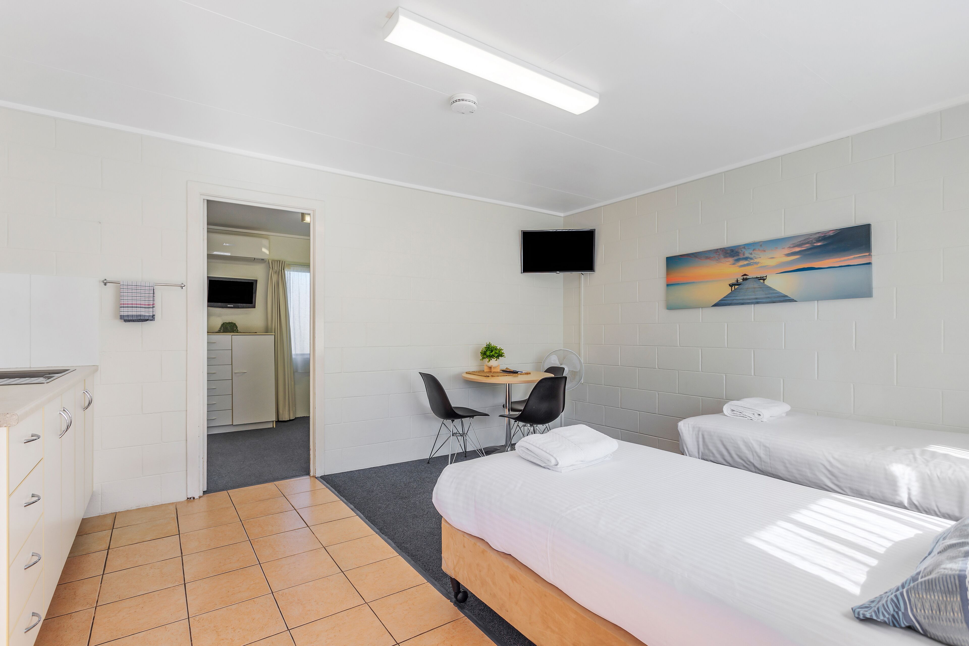 Una habitación de hotel con dos camas, un escritorio con sillas, un televisor y un cuadro en la pared.