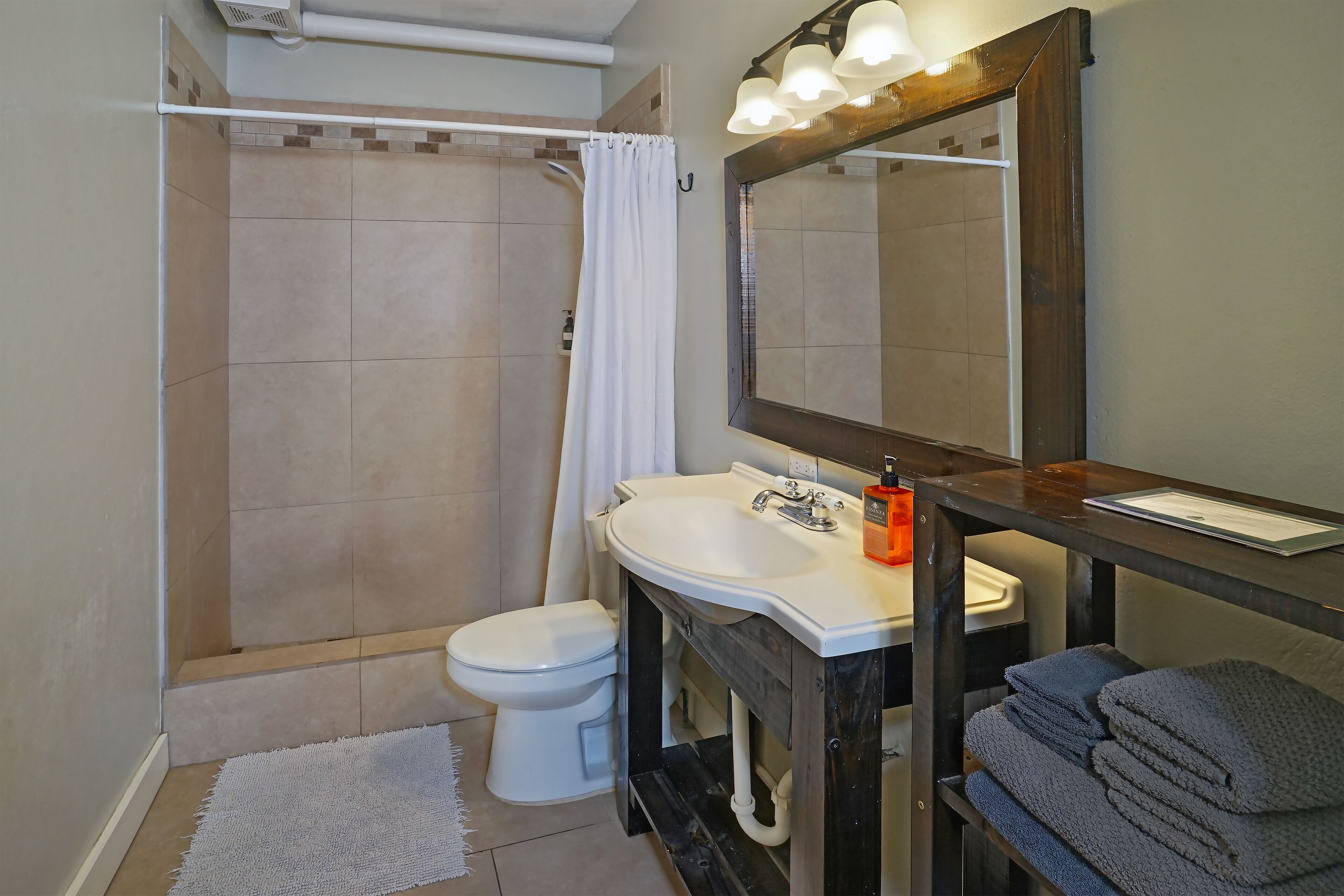 A bathroom with a shower, toilet, sink, and a mirror with lights.