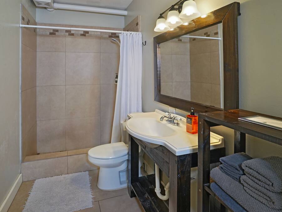 A bathroom with a shower, toilet, sink, and a mirror with lights.