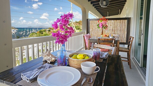 A balcony with a table set for breakfast, overlooking a marina with boats and a clear sky. - Two Sandals – A Boutique Hotel (St. Thomas)