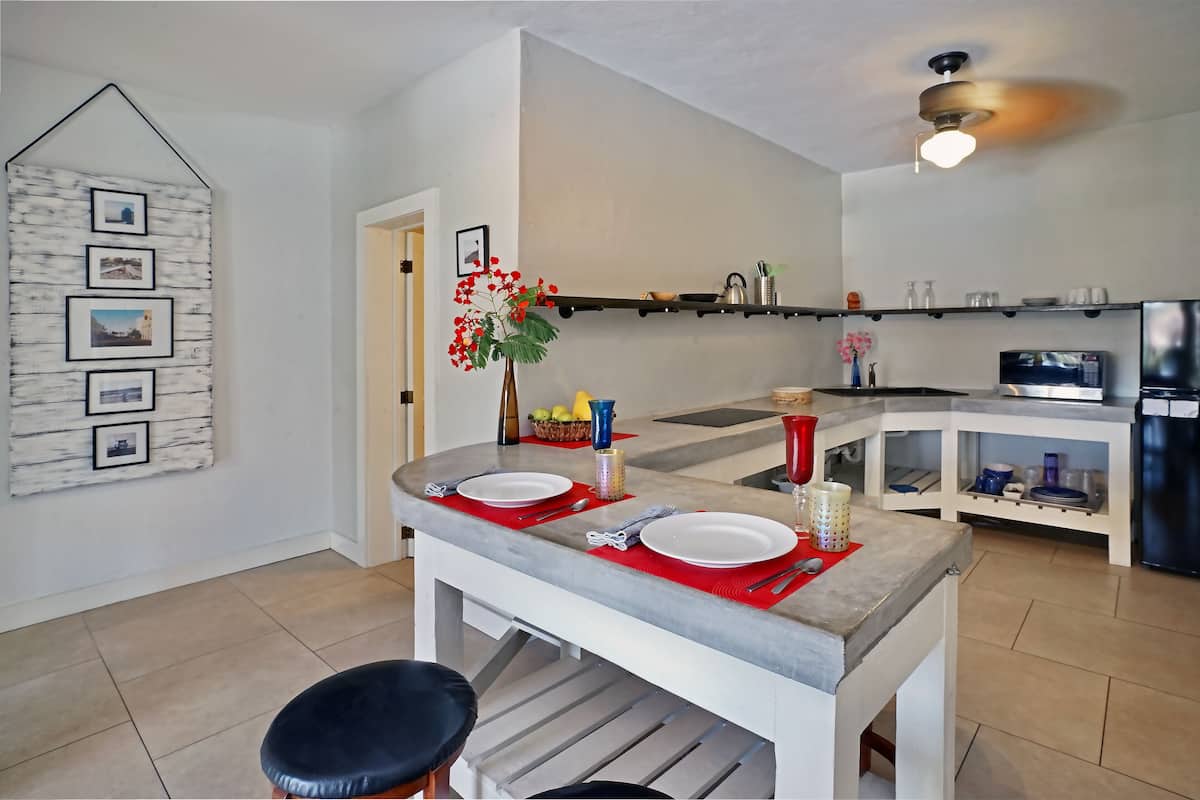 Eine moderne Küche mit Essbereich, ausgestattet mit einer Marmorarbeitsplatte, einem Deckenventilator und einem an der Wand befestigten Regal mit Küchenutensilien.
