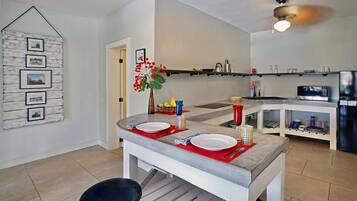 A modern kitchen with a dining area, featuring a marble countertop, a ceiling fan, and a wall-mounted shelf with kitchen items.