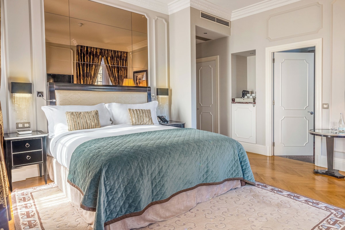 A spacious bedroom with a large bed, a nightstand, a bedside table, and a mirror.