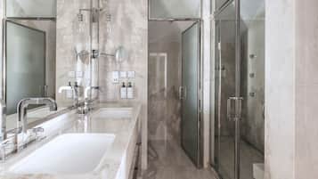 Un baño moderno con dos lavamanos, cabina de ducha con vidrio y paredes de mármol.