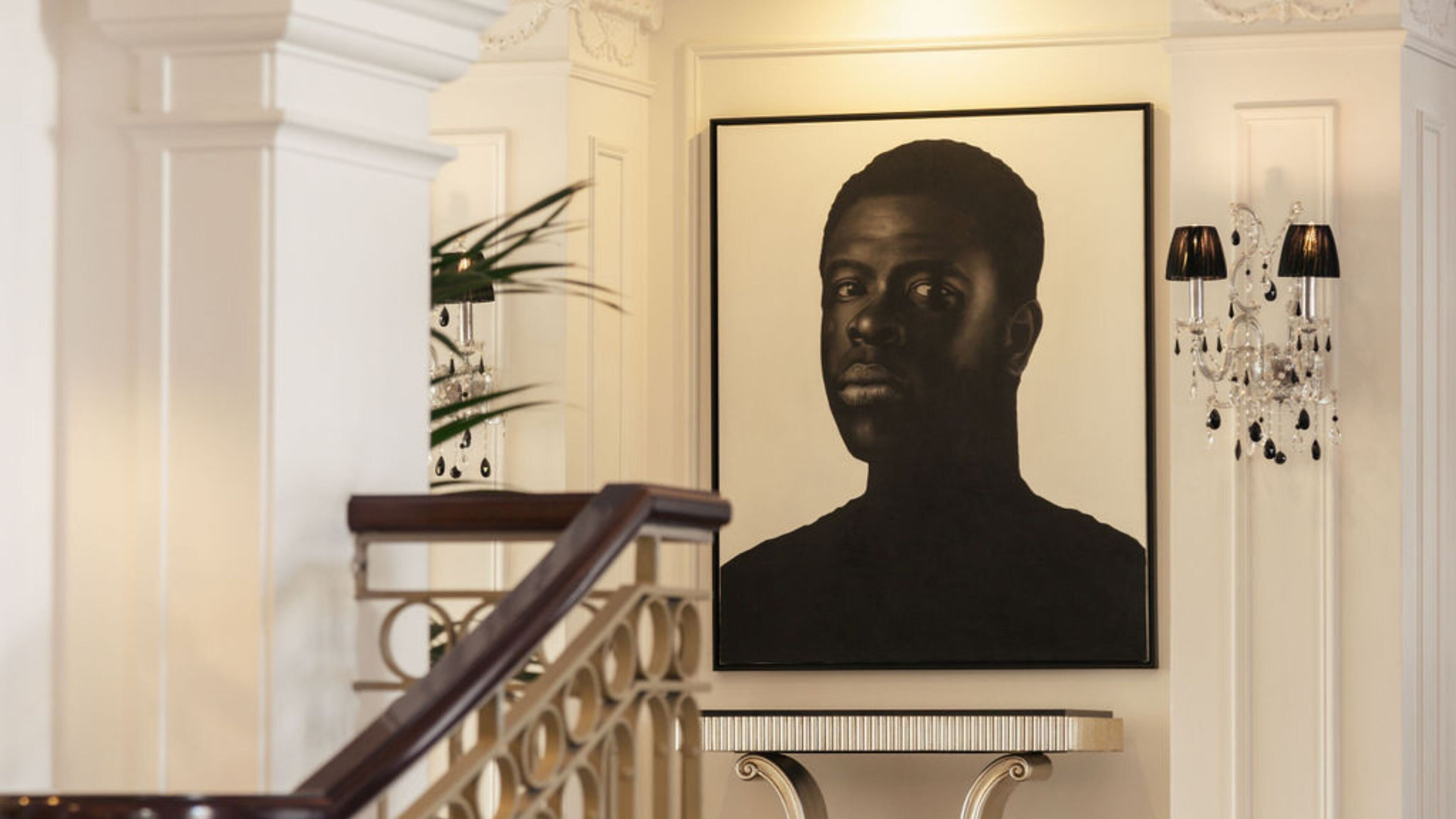 A staircase with a handrail, a framed portrait, a chandelier, and a plant.
