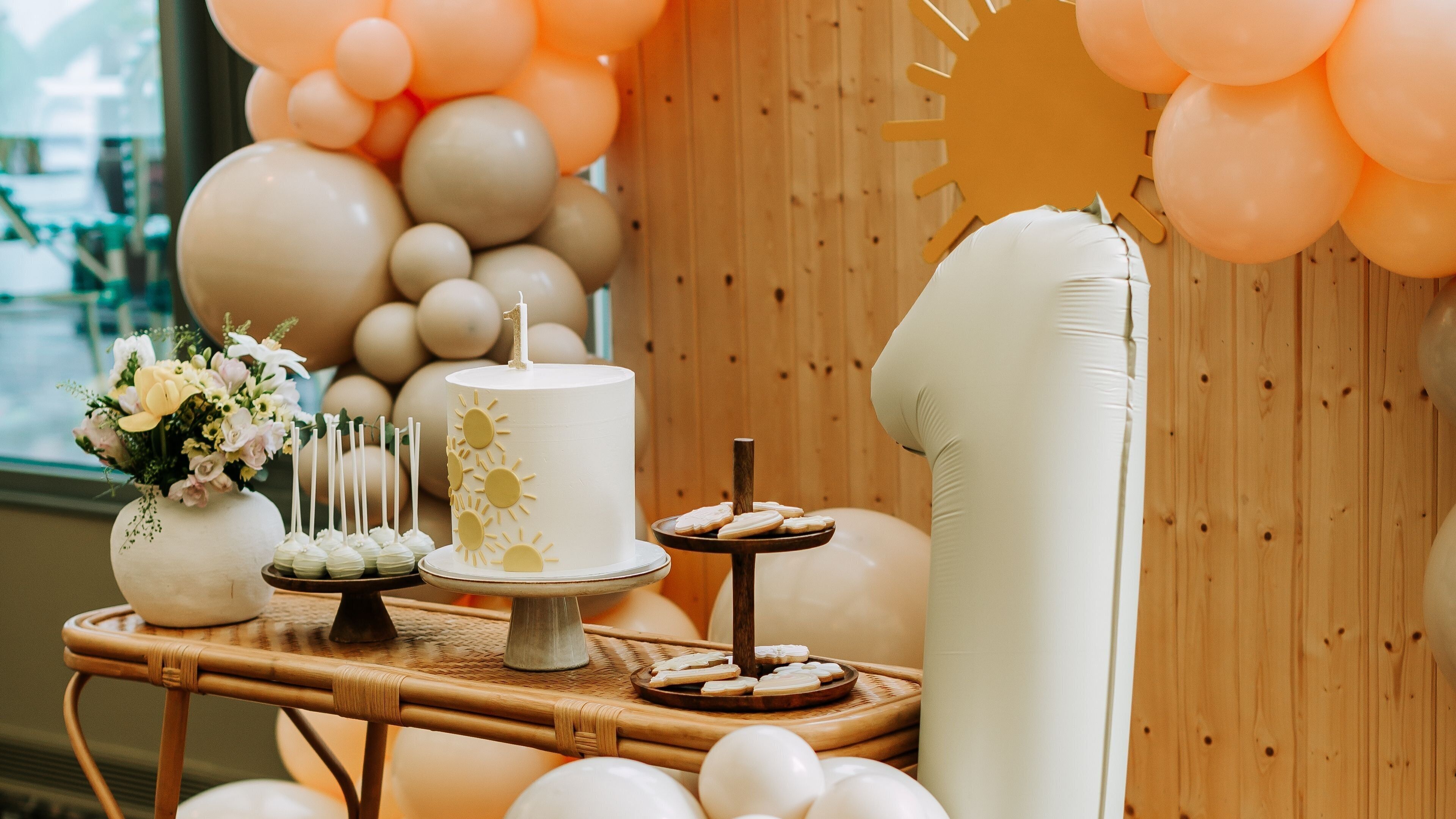 A decorated event space with a cake, cookies, and a floral arrangement on a table.