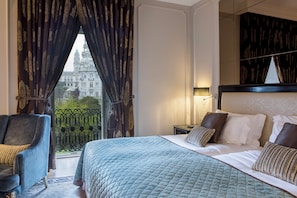 A hotel room with a large bed, a chair, a nightstand, and a view of a historic building through the window. - InterContinental Porto - Palacio das Cardosas by IHG (Porto)