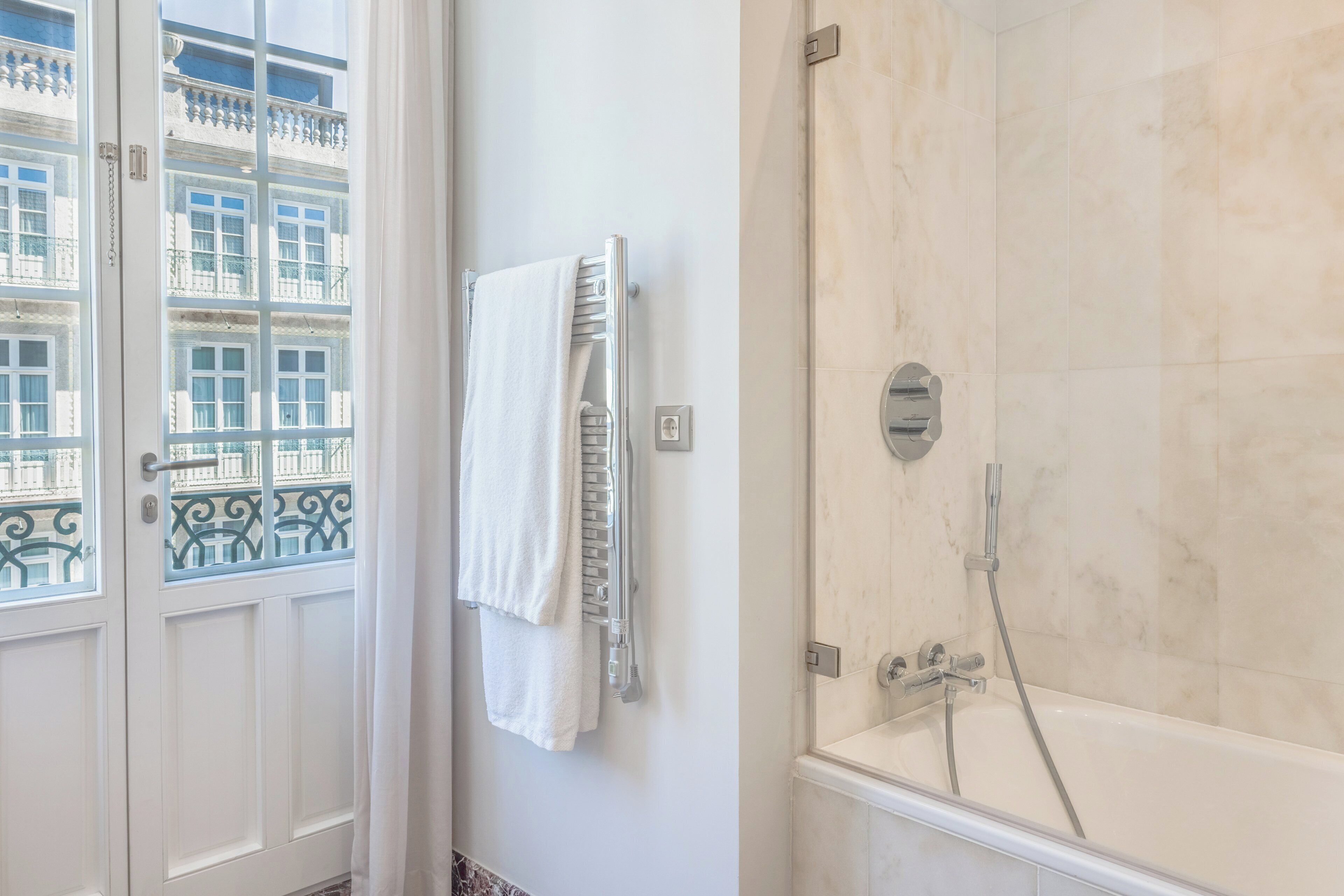 A bathroom with a bathtub, a towel rack with a towel, and a window with a view of buildings.