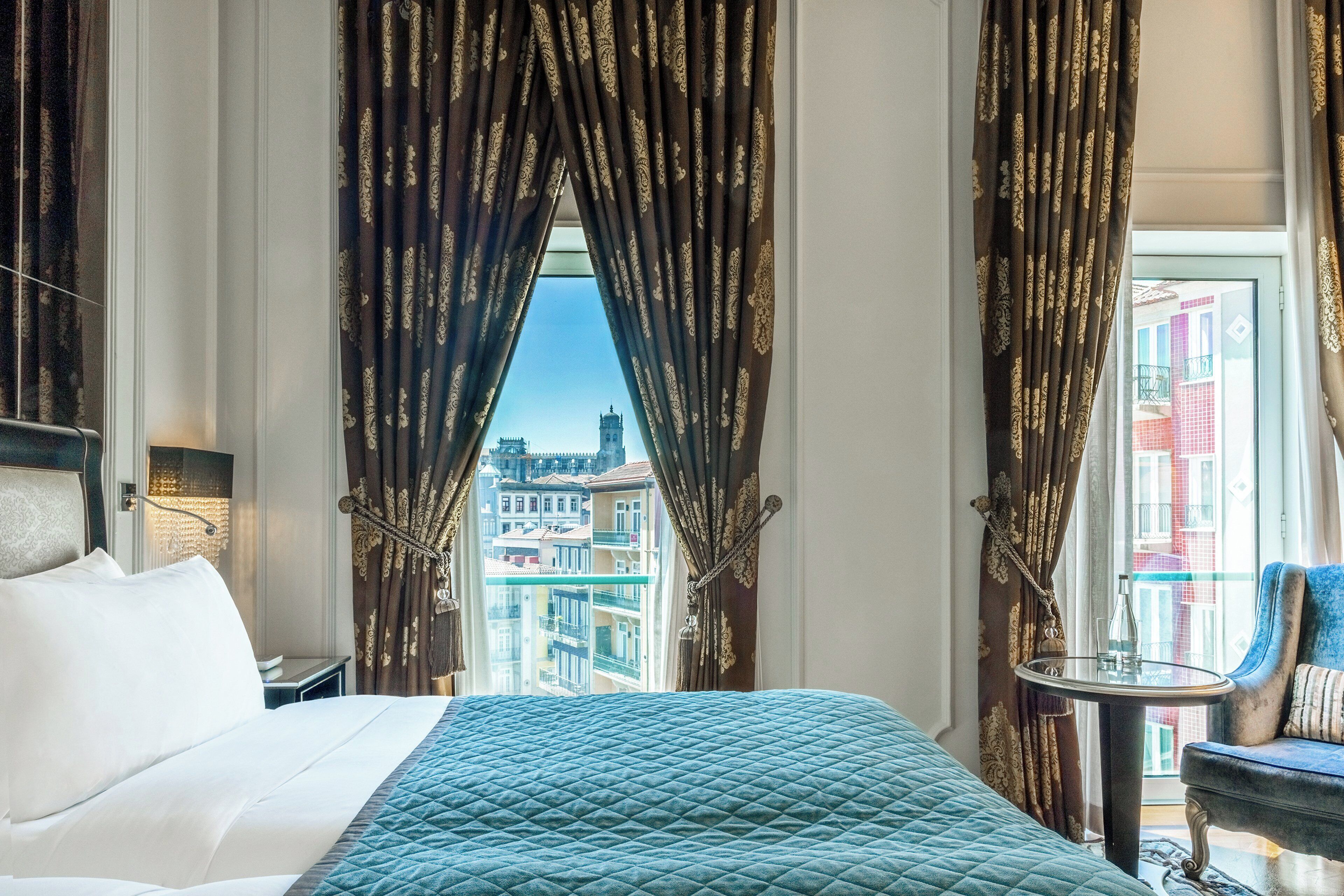 A hotel room with a large bed, a small table, and a view of buildings through the window.