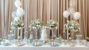 A table set with white and blue desserts, white flowers, and clear glass candle holders against a backdrop of beige curtains.