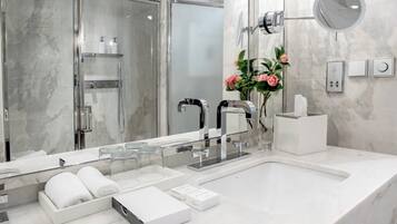 Un baño moderno con un espejo grande, cabina de ducha de vidrio y encimera de mármol.