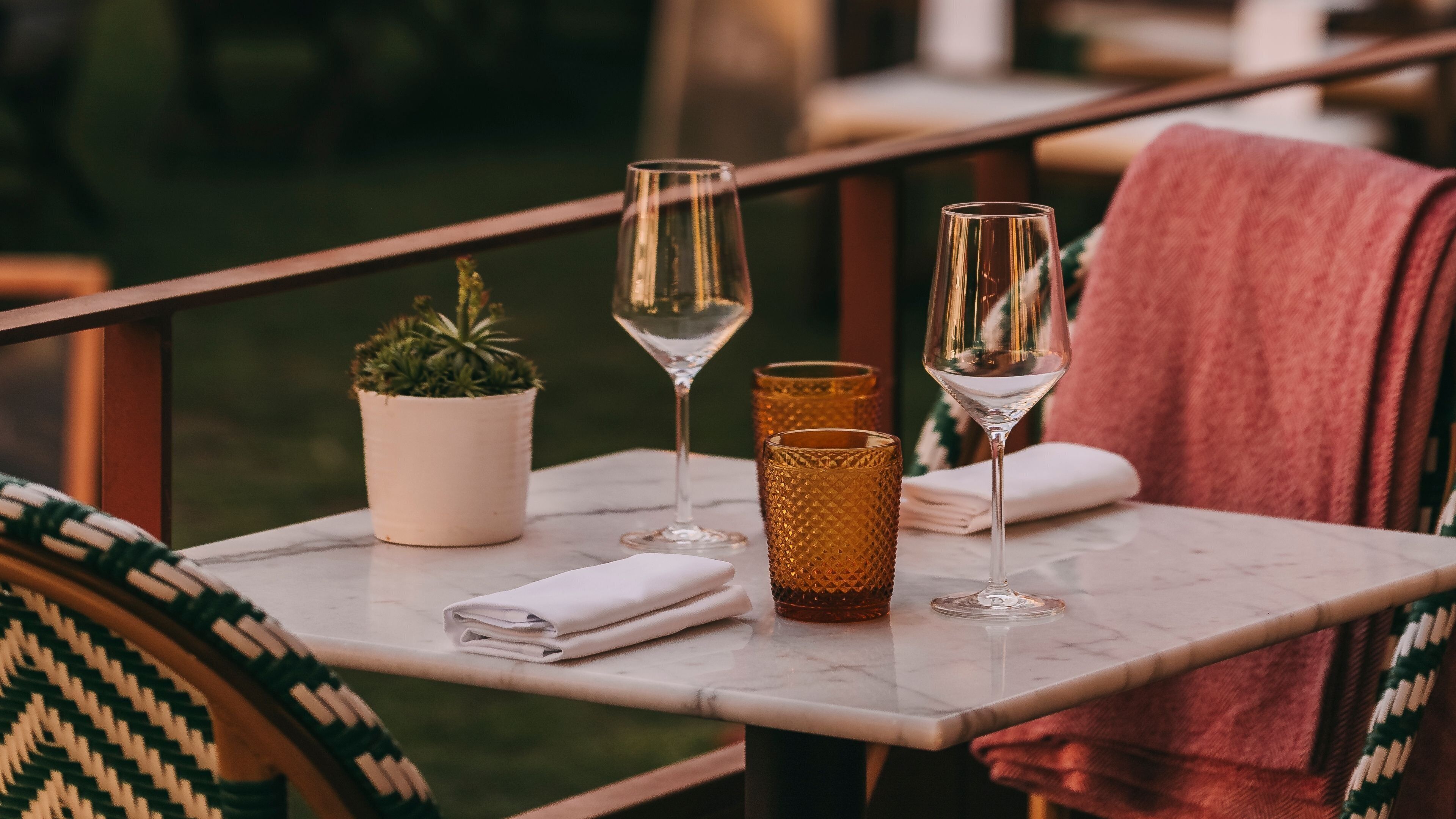 A table with two wine glasses, a small potted plant, and a textured candle holder.