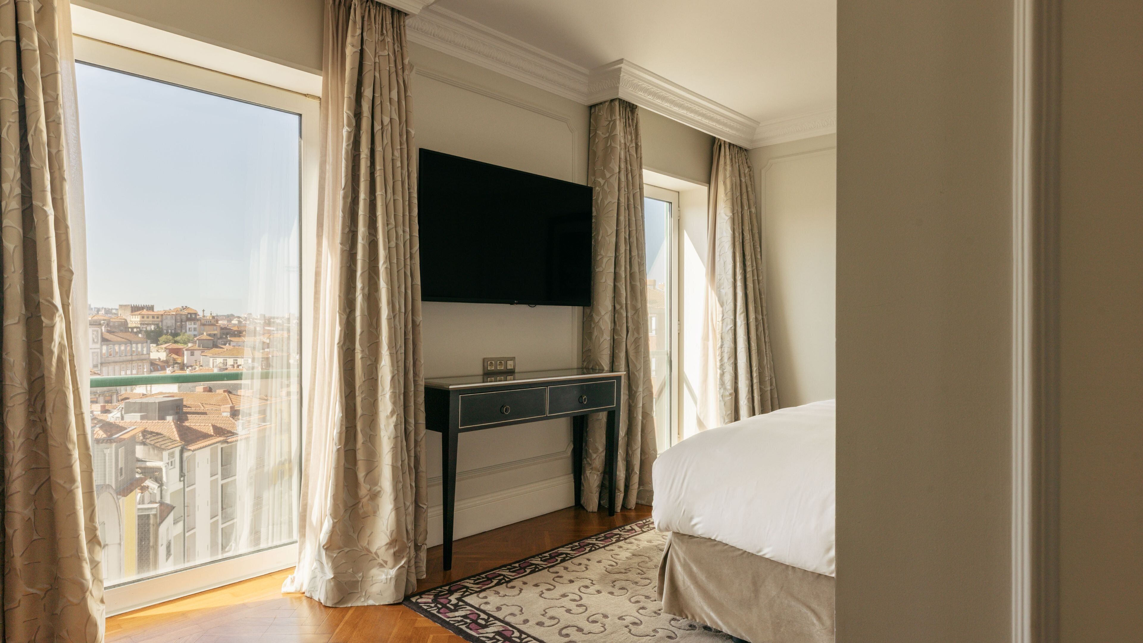 Un dormitorio con un ventanal grande, una cama, un escritorio y un televisor de pantalla plana.