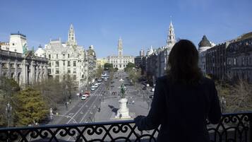 A balcony with a view of a cityscape, including historic buildings and a statue in the foreground.