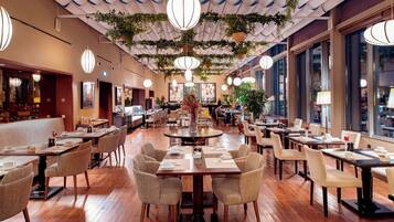 Un restaurante amplio con varias mesas y sillas, ventanas grandes y plantas colgantes.