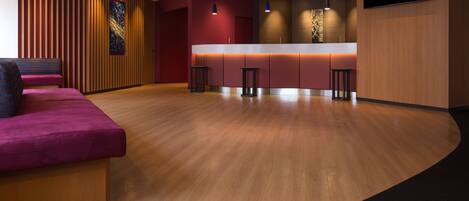Un lobby moderno con un mostrador de recepción de madera, una zona de estar con un sofá rosa y un suelo alfombrado en color negro.