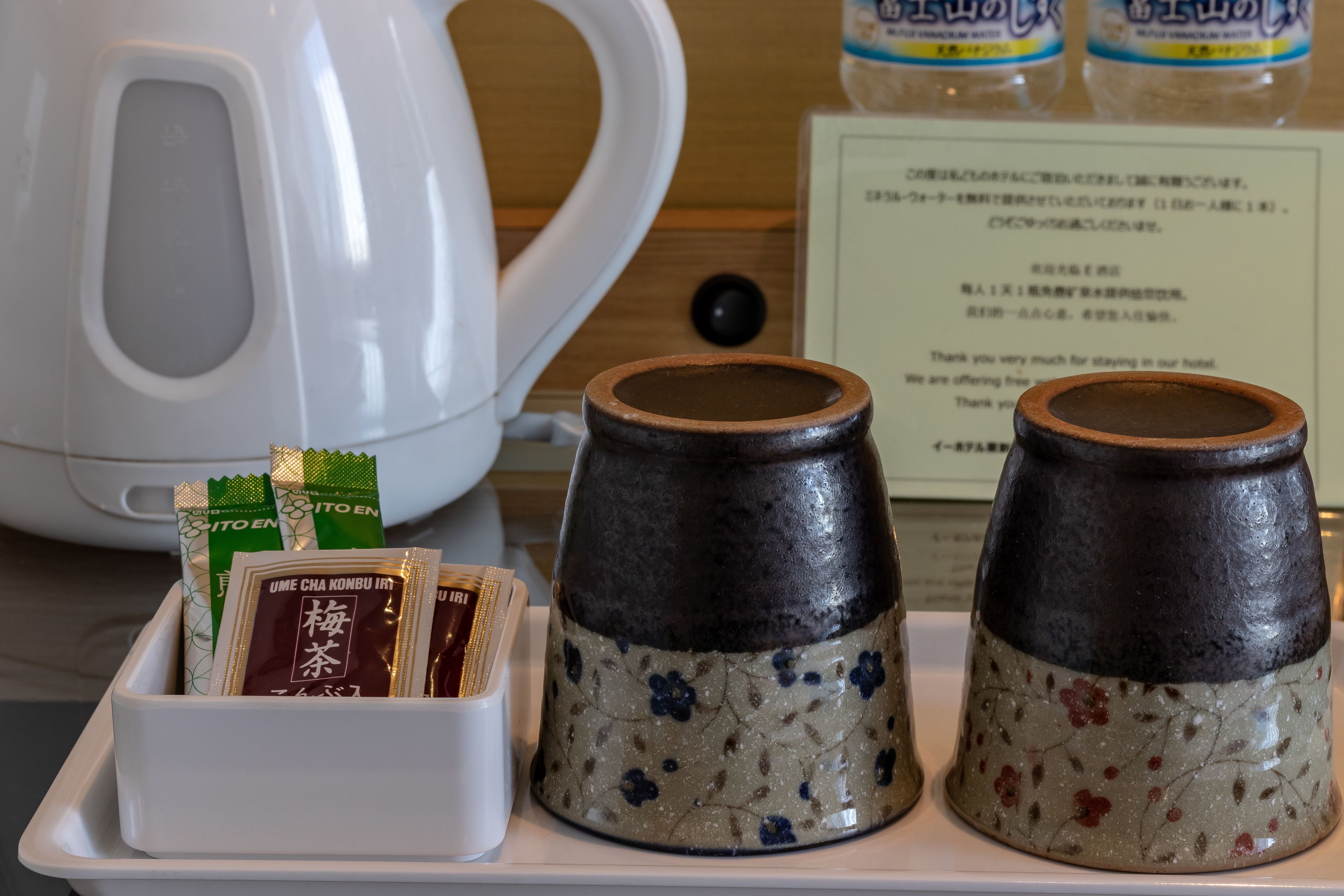 A tray with tea packets, a white kettle, and two ceramic containers with floral patterns.