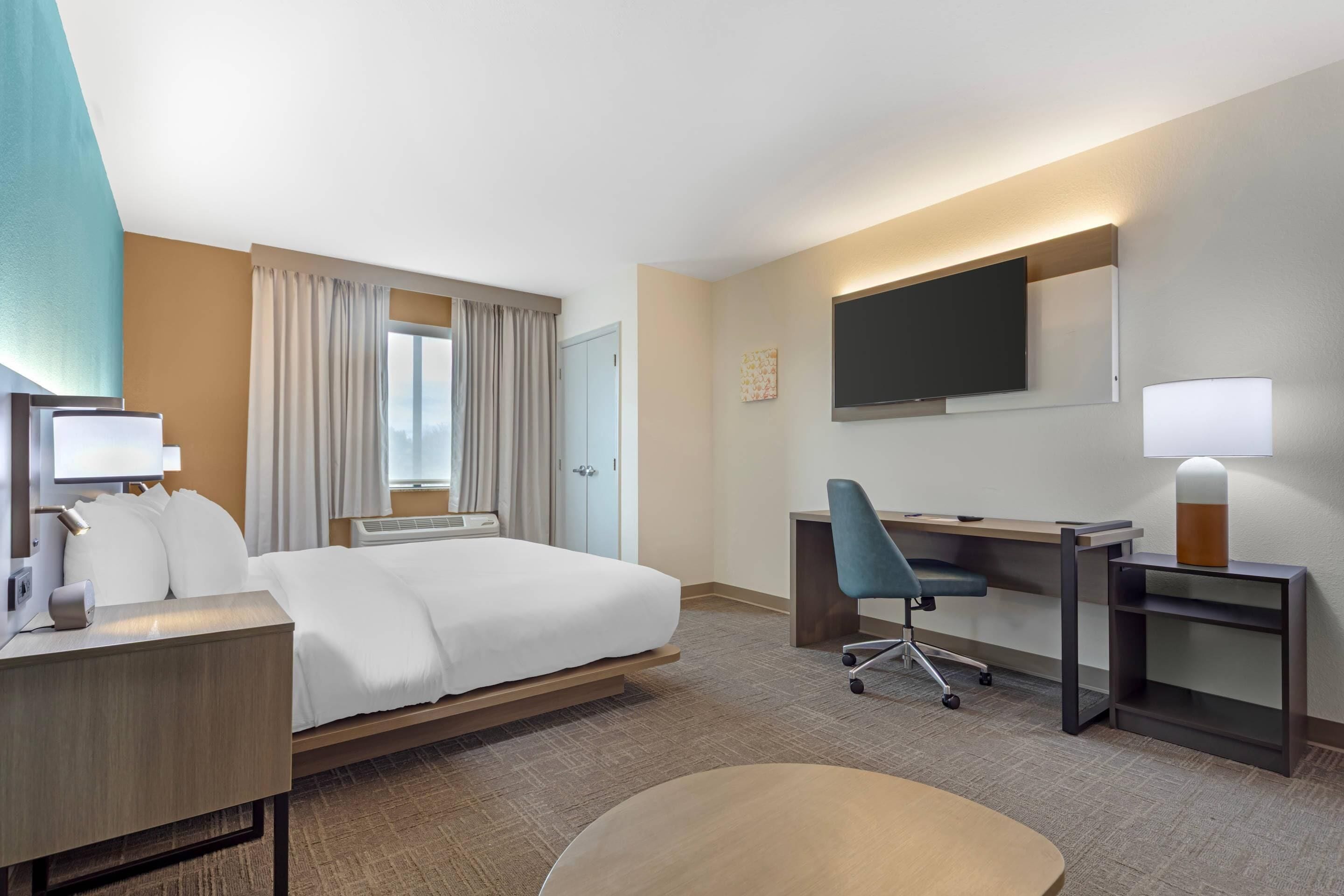 Une chambre d’hôtel équipée d’un lit, d’un bureau, d’une chaise, d’une télévision et d’une fenêtre avec des rideaux.