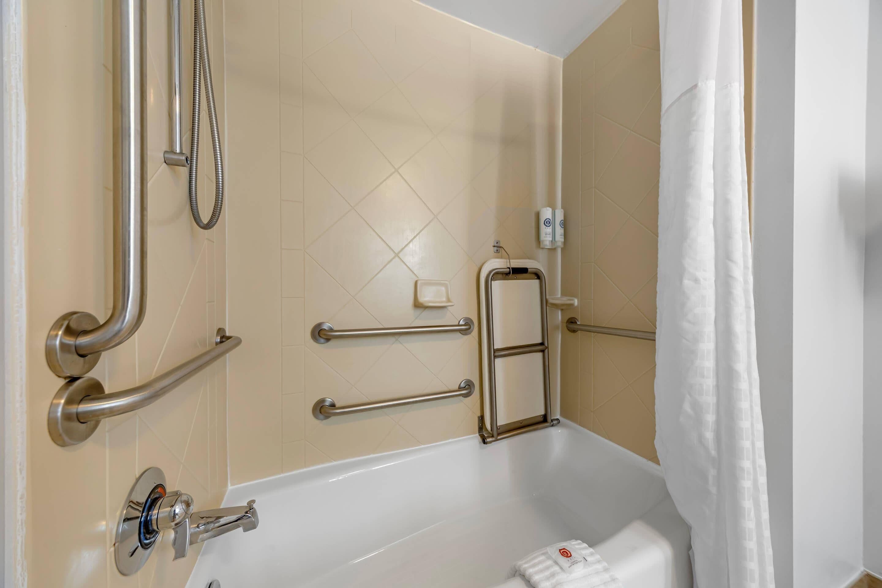 Une salle de bain équipée d’une baignoire, de barres d’appui, d’un flexible de douche et d’un porte-serviettes.