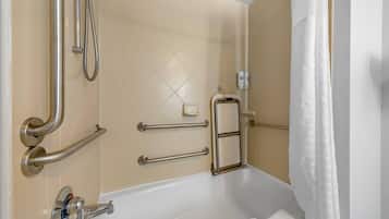 Une salle de bain équipée d’une baignoire, de barres d’appui, d’un flexible de douche et d’un porte-serviettes.