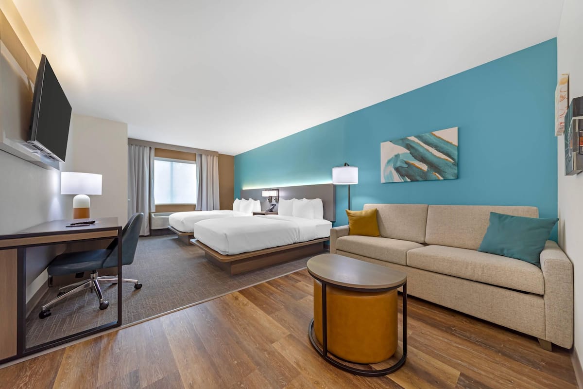 A hotel room with a bed, a desk, a chair, a sofa, and a lamp.