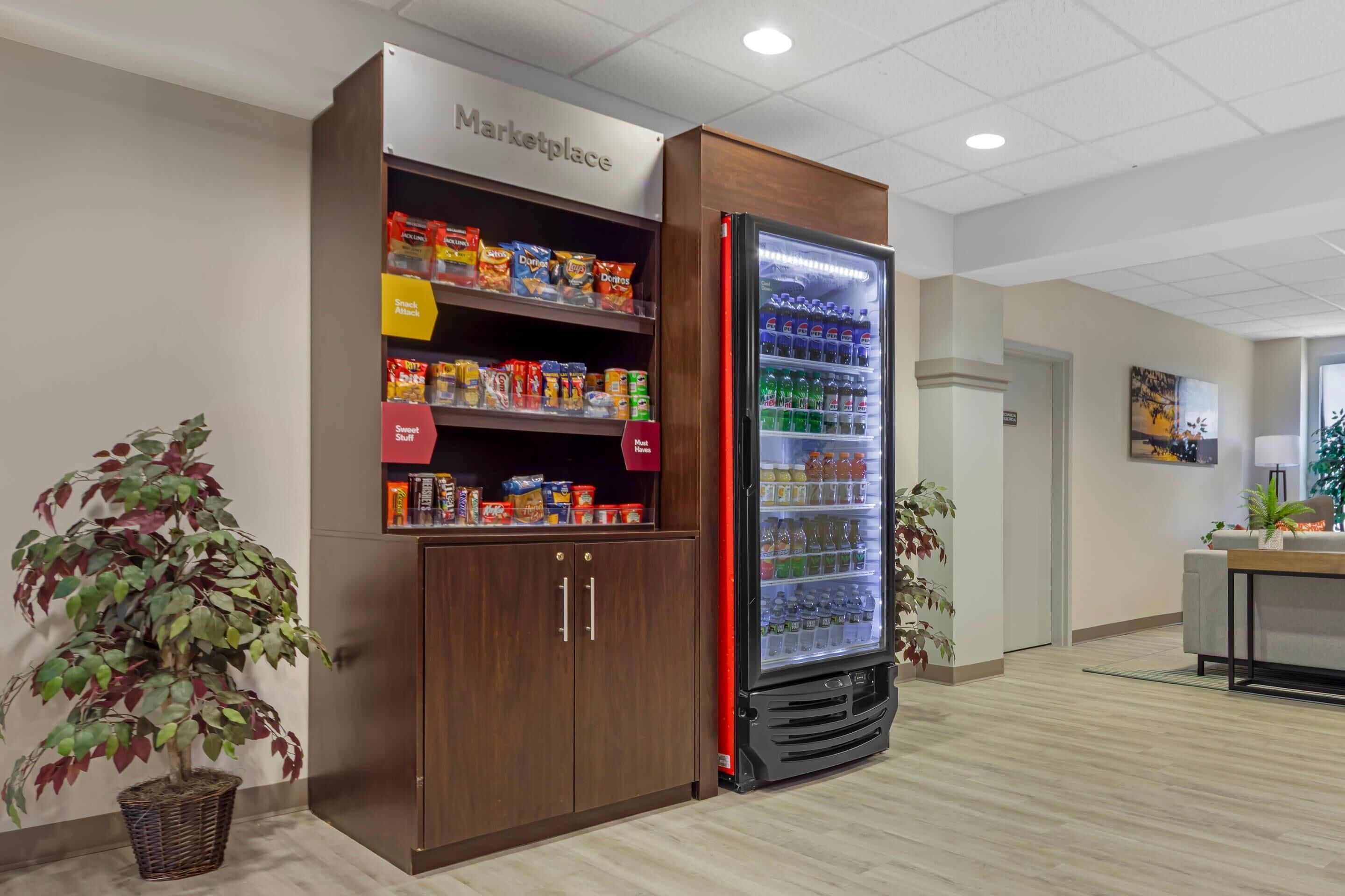 A kitchenette area with a refrigerator stocked with beverages and snacks, a microwave, and a small cabinet with a 'Marketplace' sign above it.