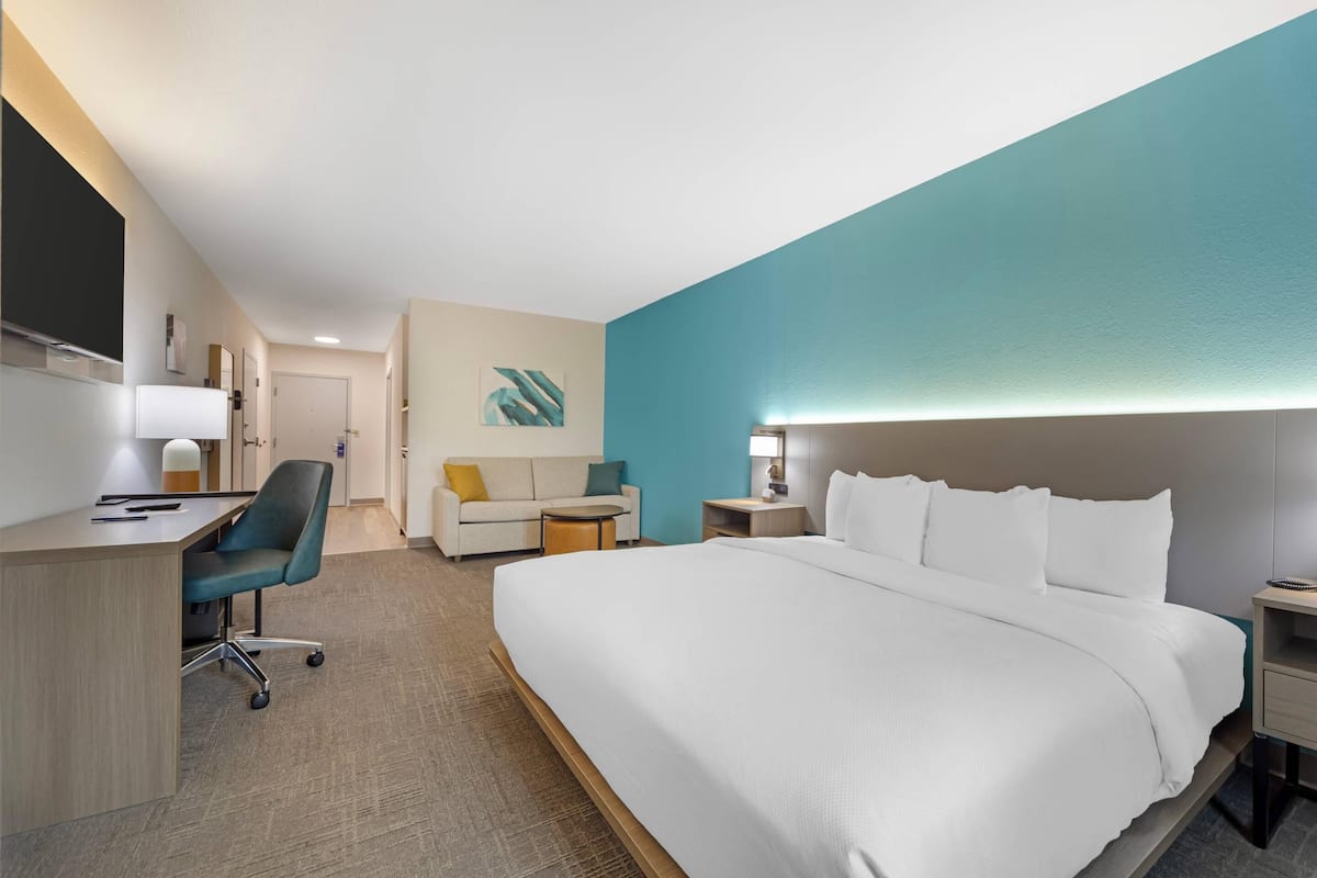 A hotel room with a large bed, a desk with a chair, a sofa, and a small table.
