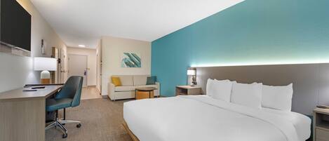 A hotel room with a large bed, a desk with a chair, a sofa, and a small table.