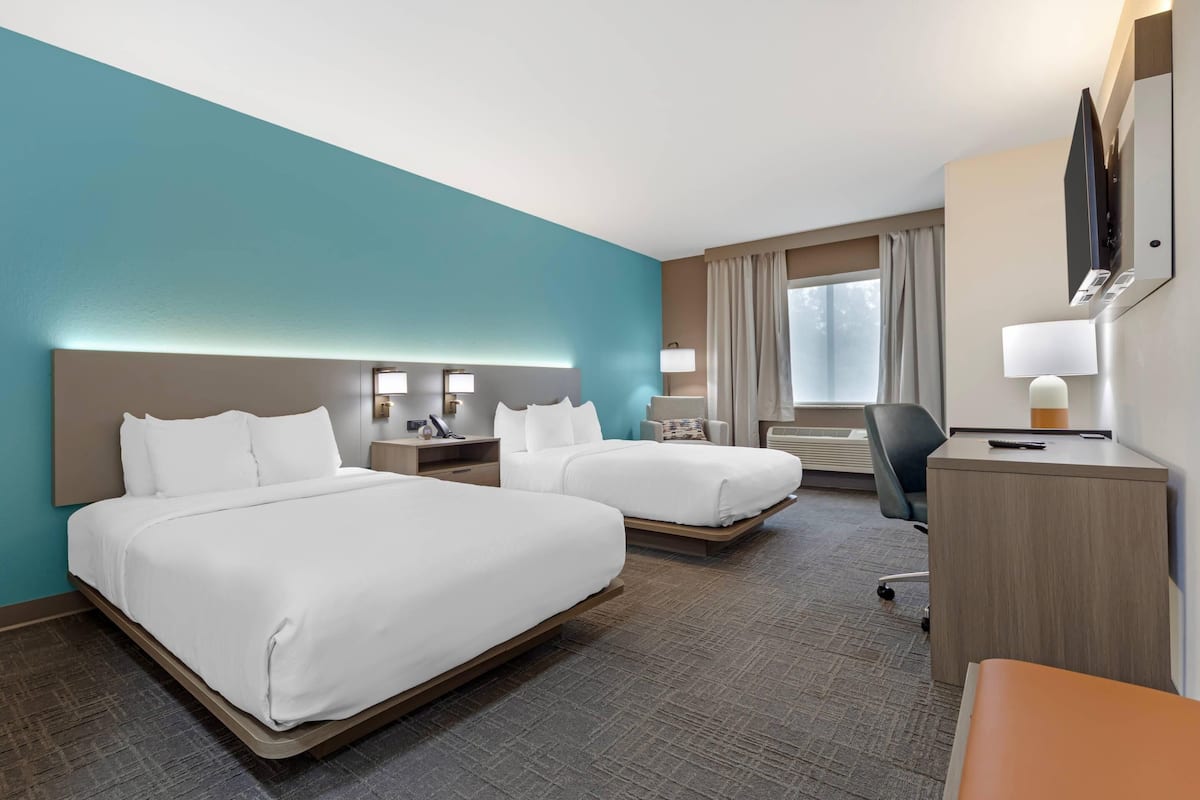 A hotel room with two beds, a desk, a chair, and a TV.
