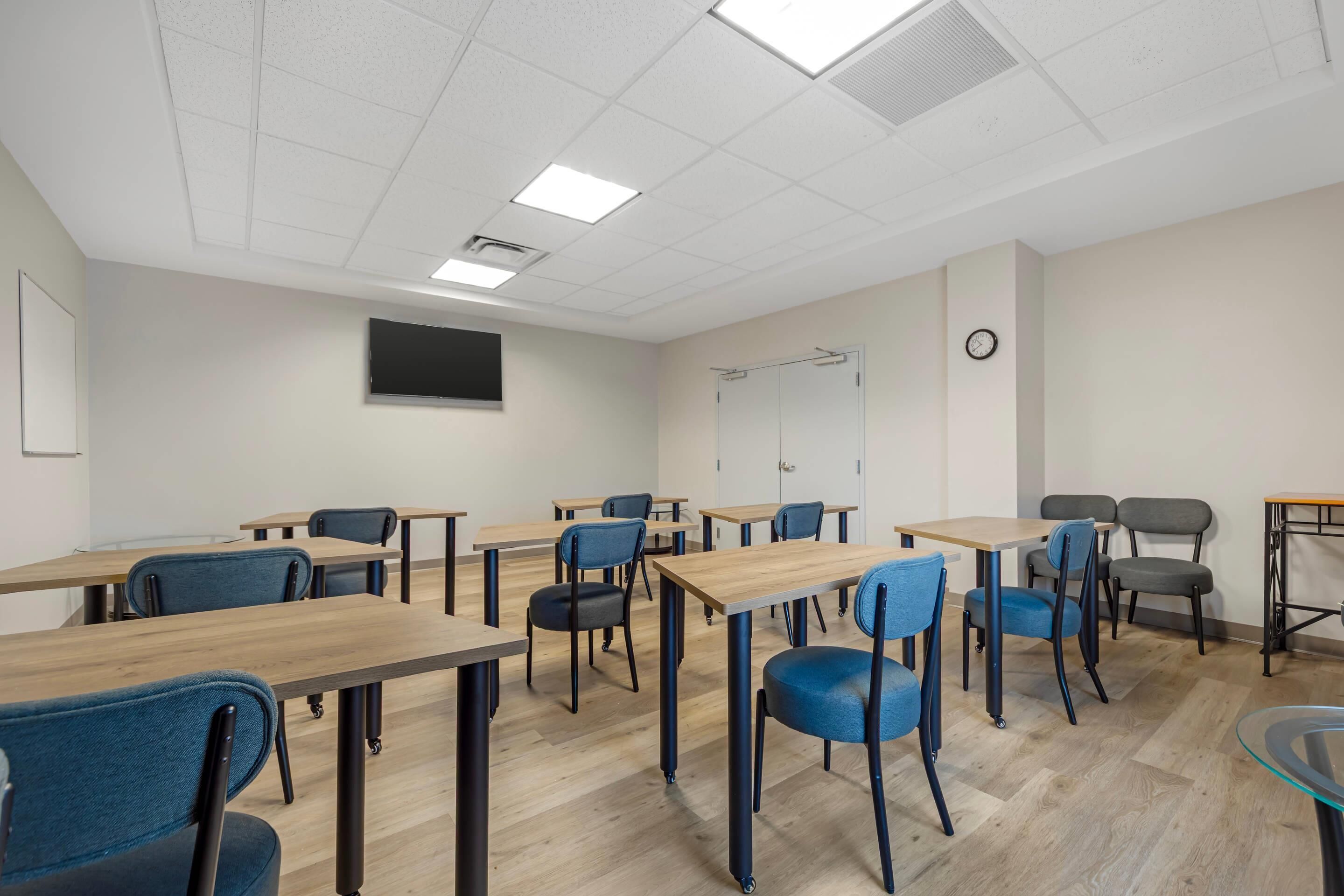 A classroom with desks, chairs, a clock, and a television on the wall.