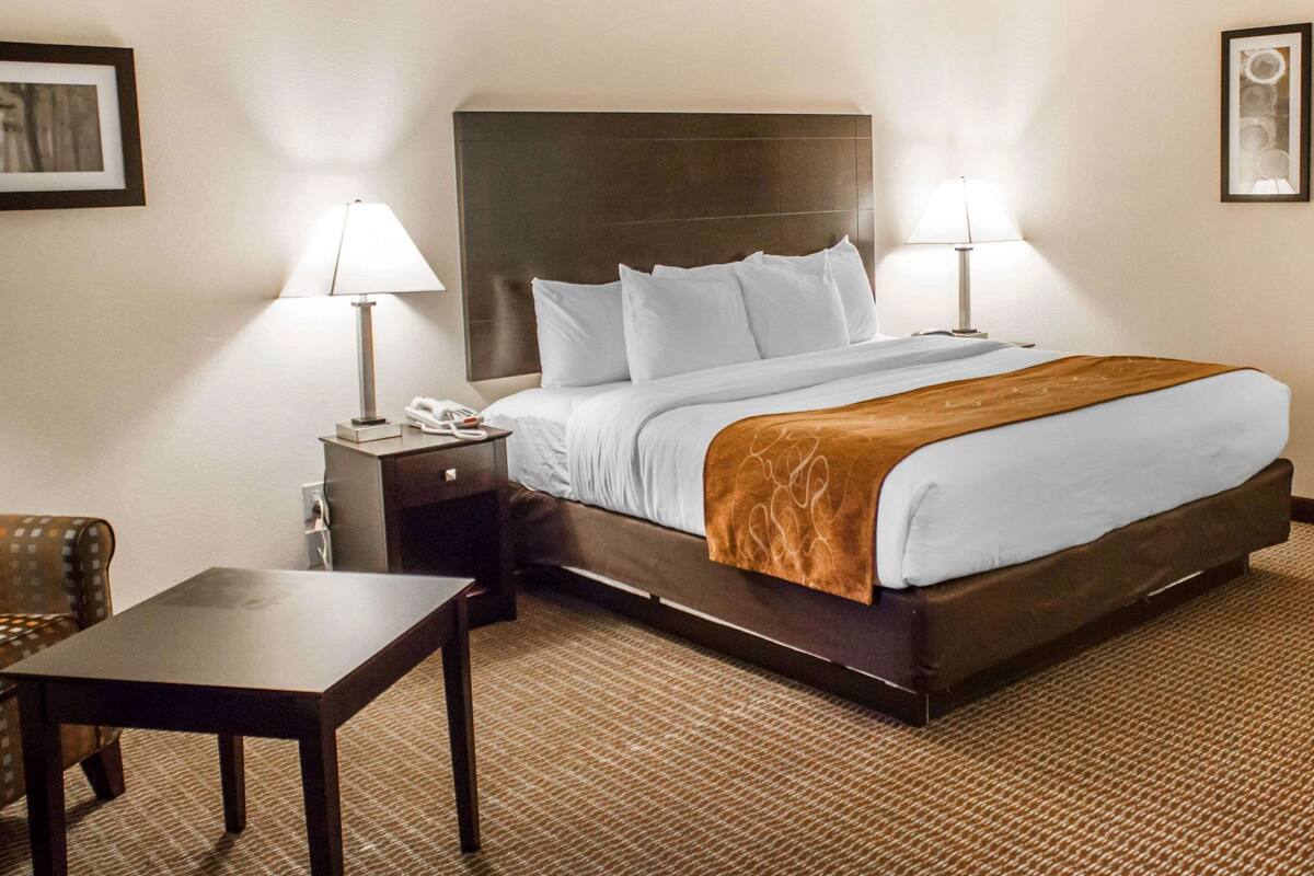 A hotel room with a large bed, two bedside tables, a nightstand, a chair, and a carpeted floor.