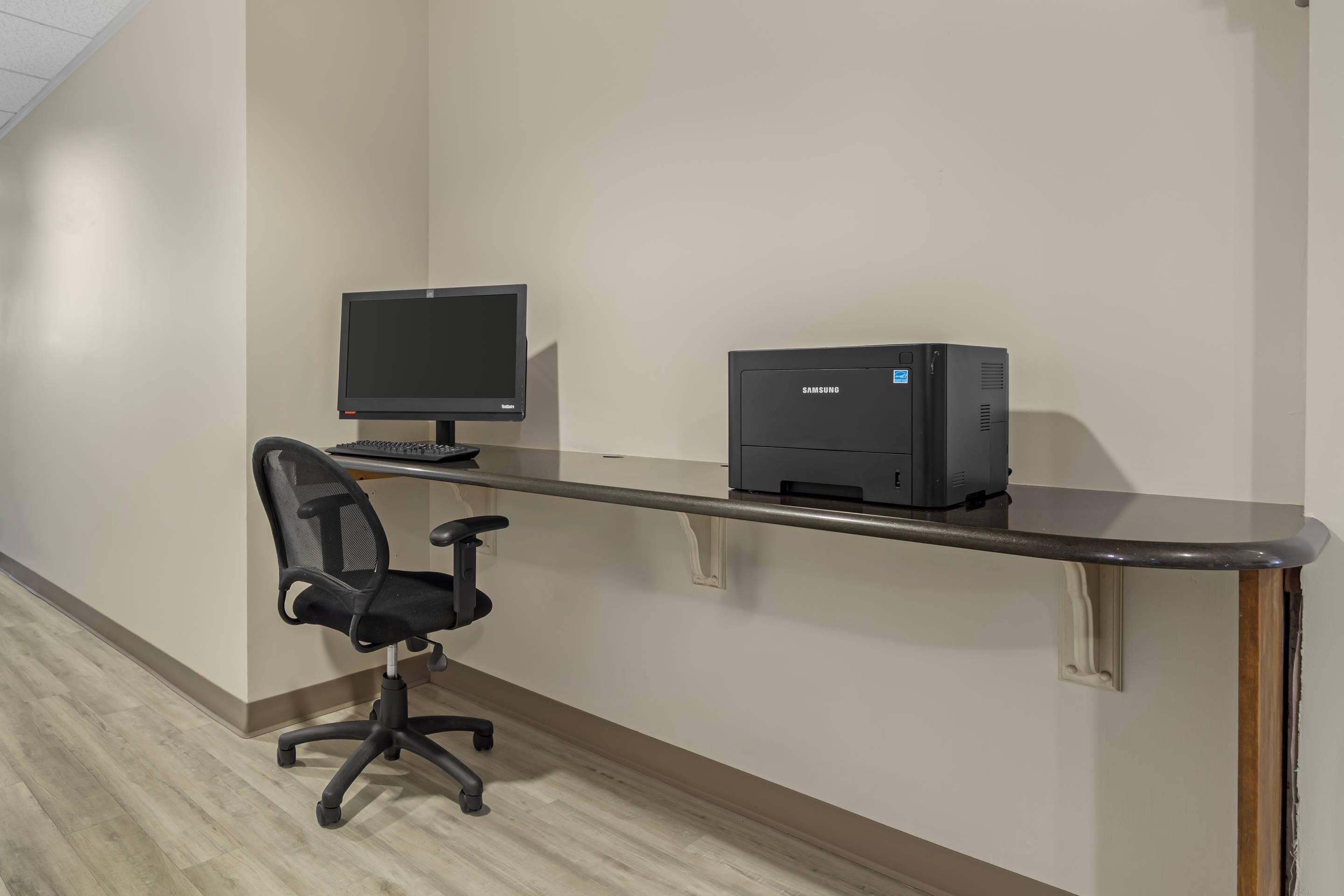 Un espacio de trabajo con un monitor de computadora, una impresora y una silla de oficina.