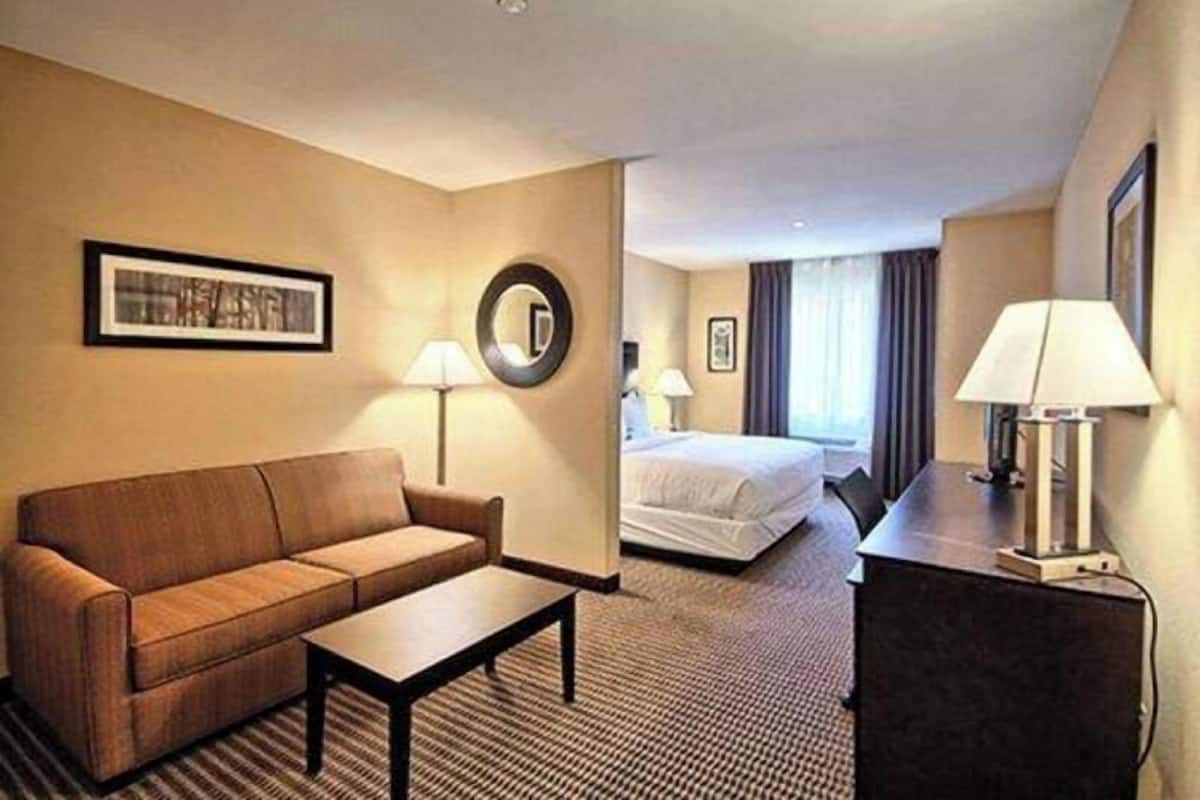 A hotel room with a sofa, a bed, a desk, a lamp, and a mirror.