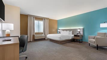 A hotel room with a bed, desk, chair, bedside table, lamp, and a window with curtains.