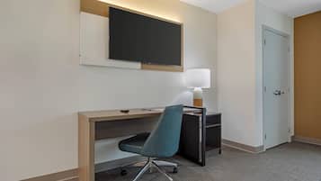 A hotel room with a desk, chair, TV, lamp, and a door.