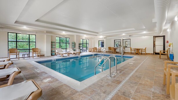 A large indoor swimming pool with lounge chairs and tables, surrounded by large windows. - Comfort Suites Lewisburg near University (Lewisburg)