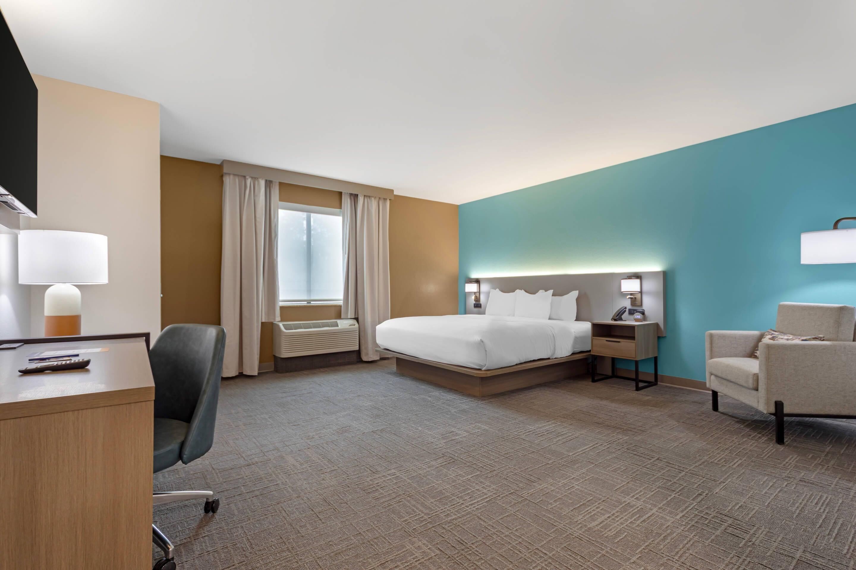 A hotel room with a bed, desk, chair, and a window with curtains.
