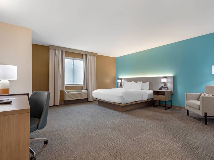 A hotel room with a bed, desk, chair, and a window with curtains.