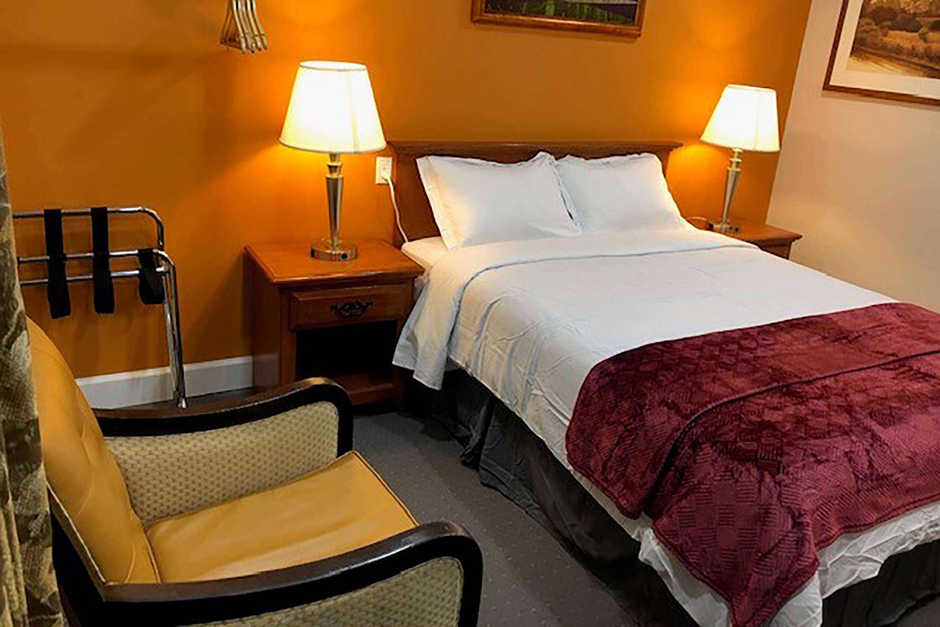A hotel room with a bed, two bedside lamps, a chair, and a nightstand.