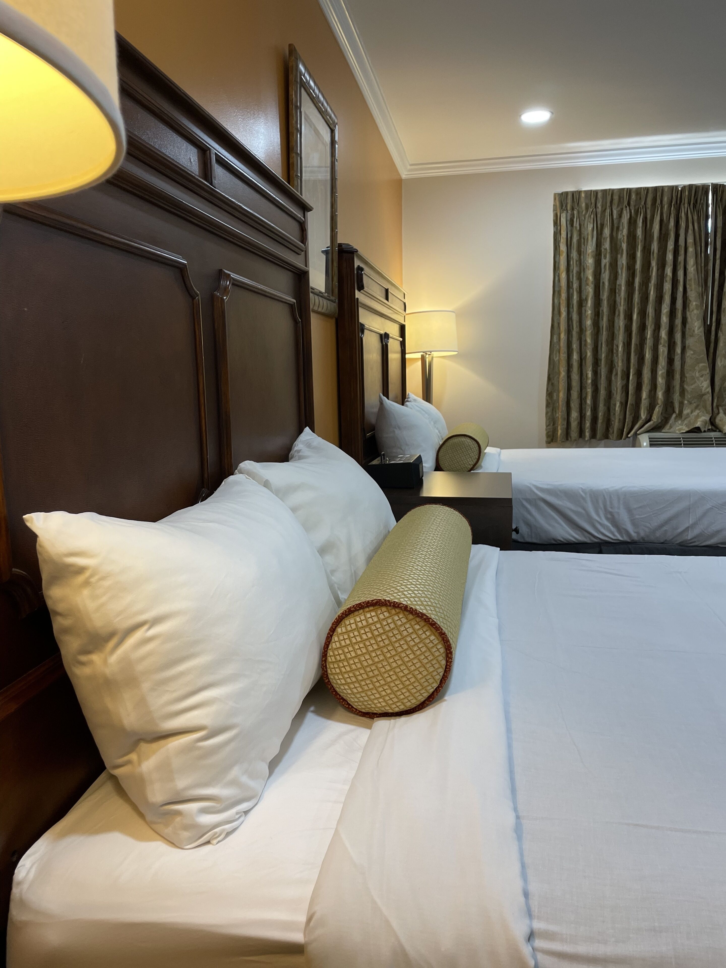A hotel room with two beds, a wooden headboard, a lamp, and a curtain.