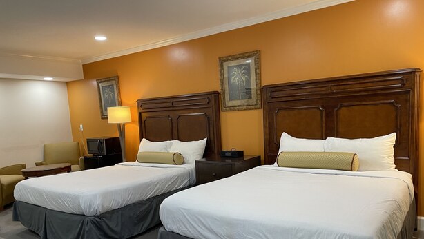 Habitación de hotel con dos camas, cada una con cabecero de madera, un escritorio, una silla y una lámpara.