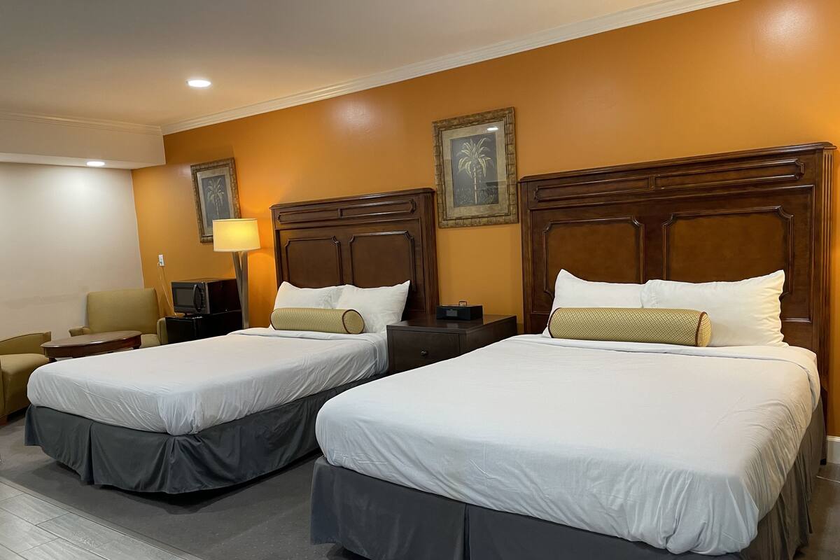 A hotel room with two beds, each with a wooden headboard, a desk, a chair, and a lamp.