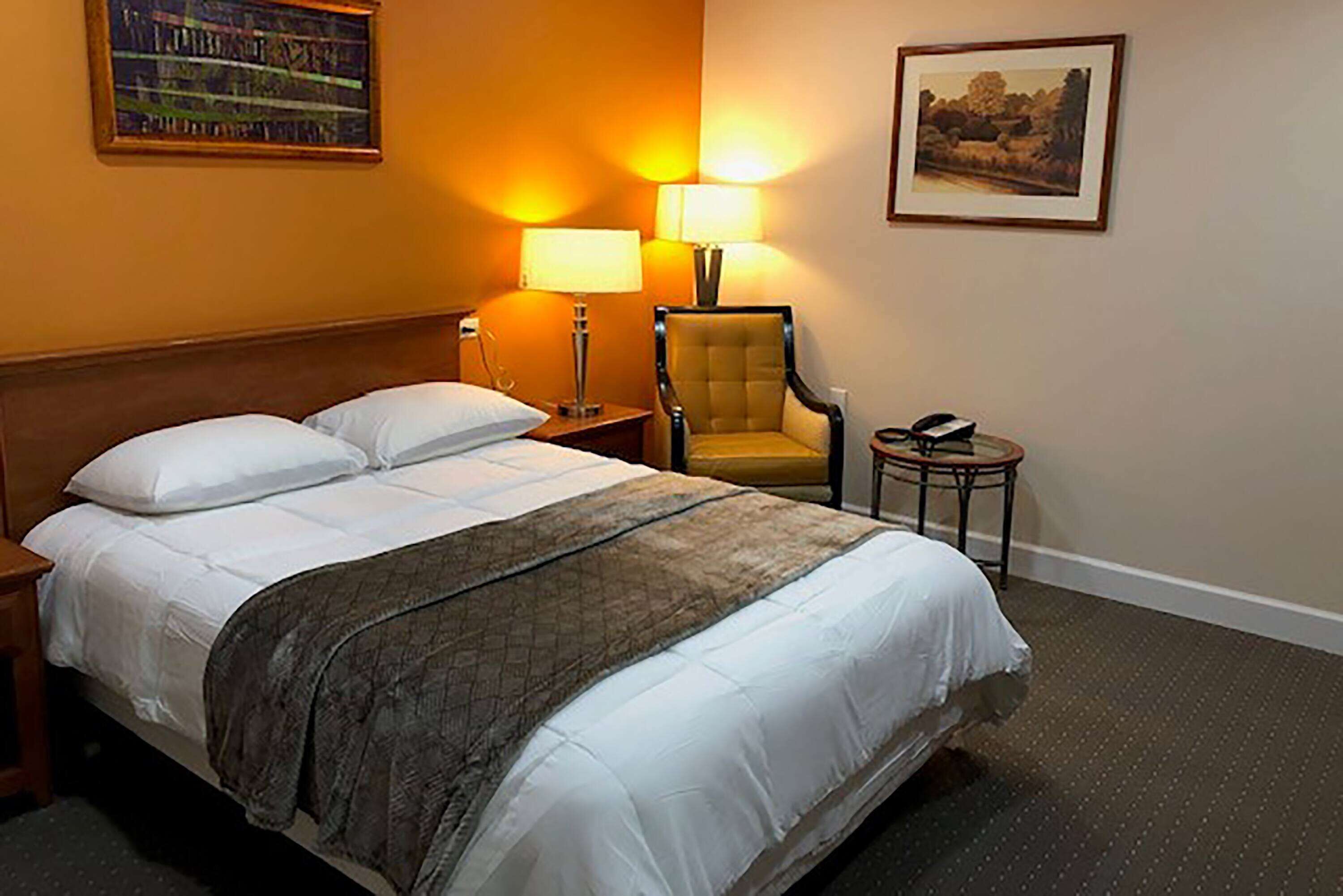 Una camera d'albergo con un letto grande, due abat-jour, una sedia, un tavolino e un quadro appeso al muro.