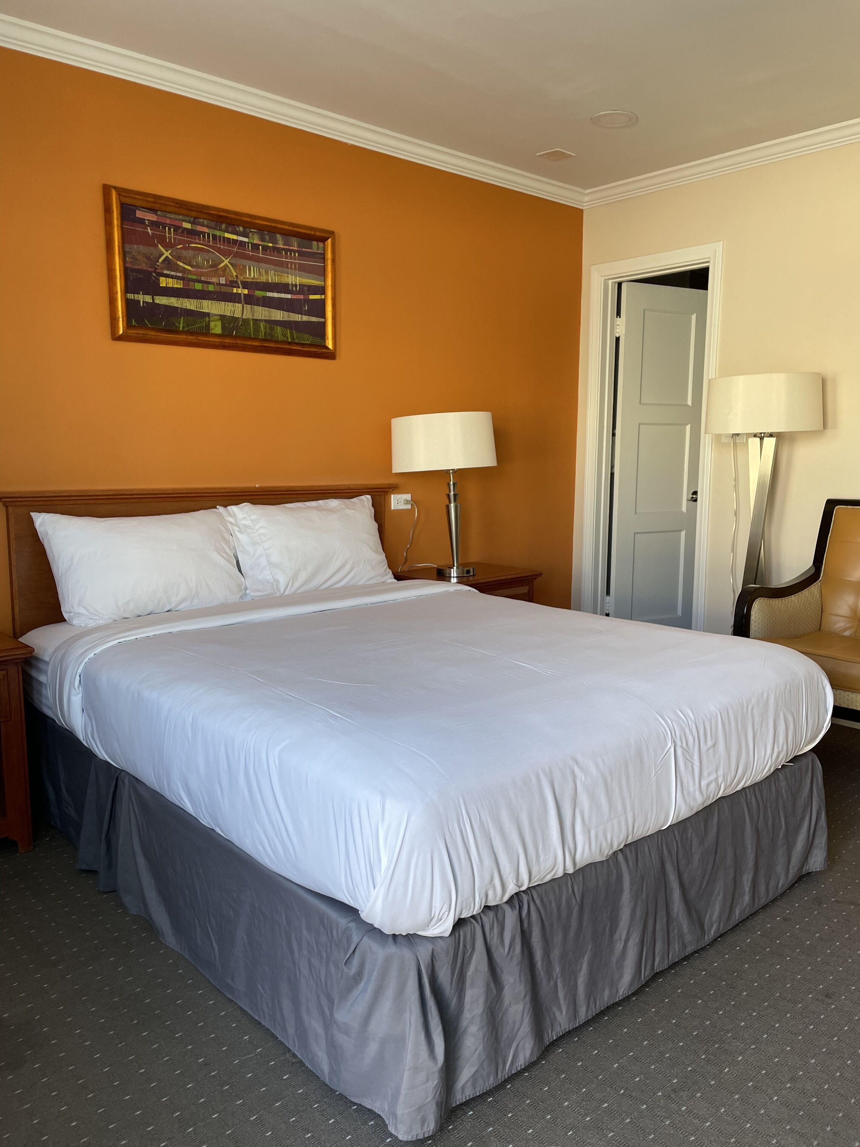 A hotel room with a large bed, two bedside lamps, a door, and a chair.