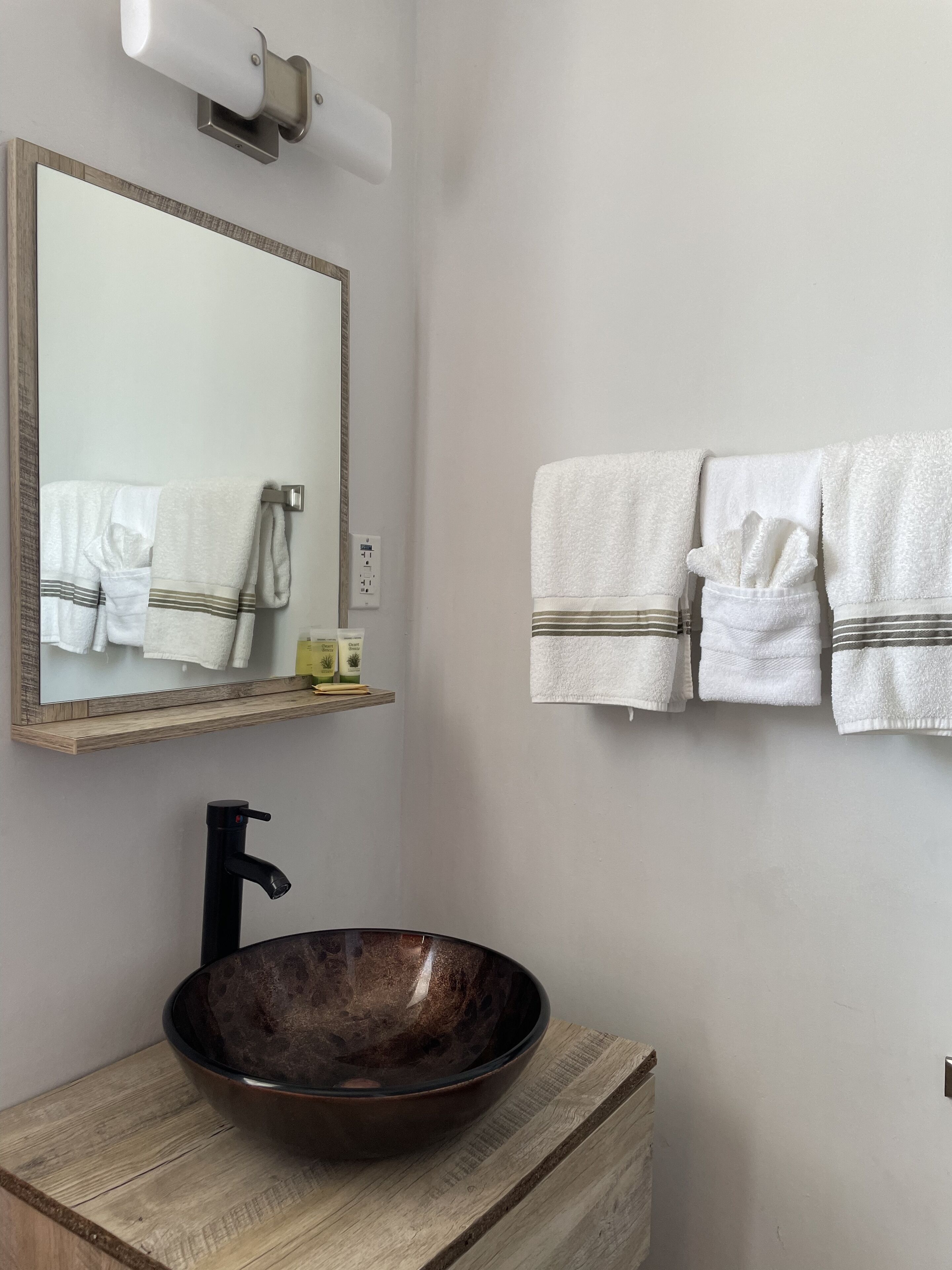 A bathroom with a wooden vanity, a large mirror, a vessel sink, and two towels hanging on the wall.